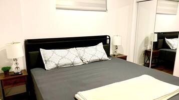 A neatly made bed with a dark headboard, two bedside lamps, and a small bedside table with a plant.