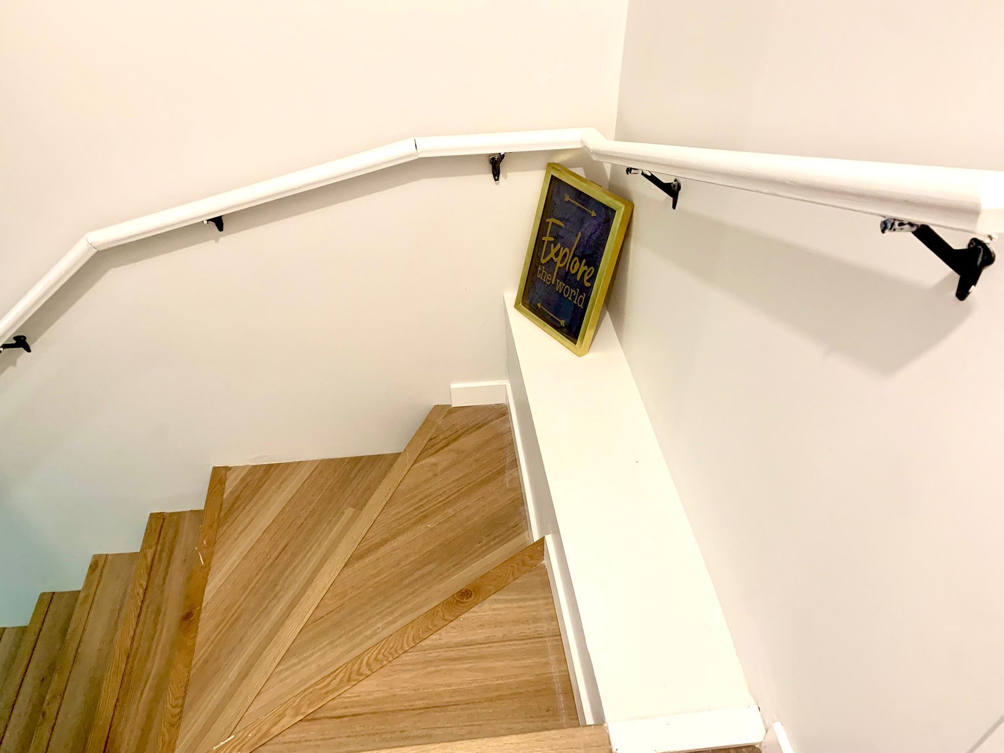 Un escalier en bois avec des rampes blanches et, sur le mur, une citation inspirante encadrée.