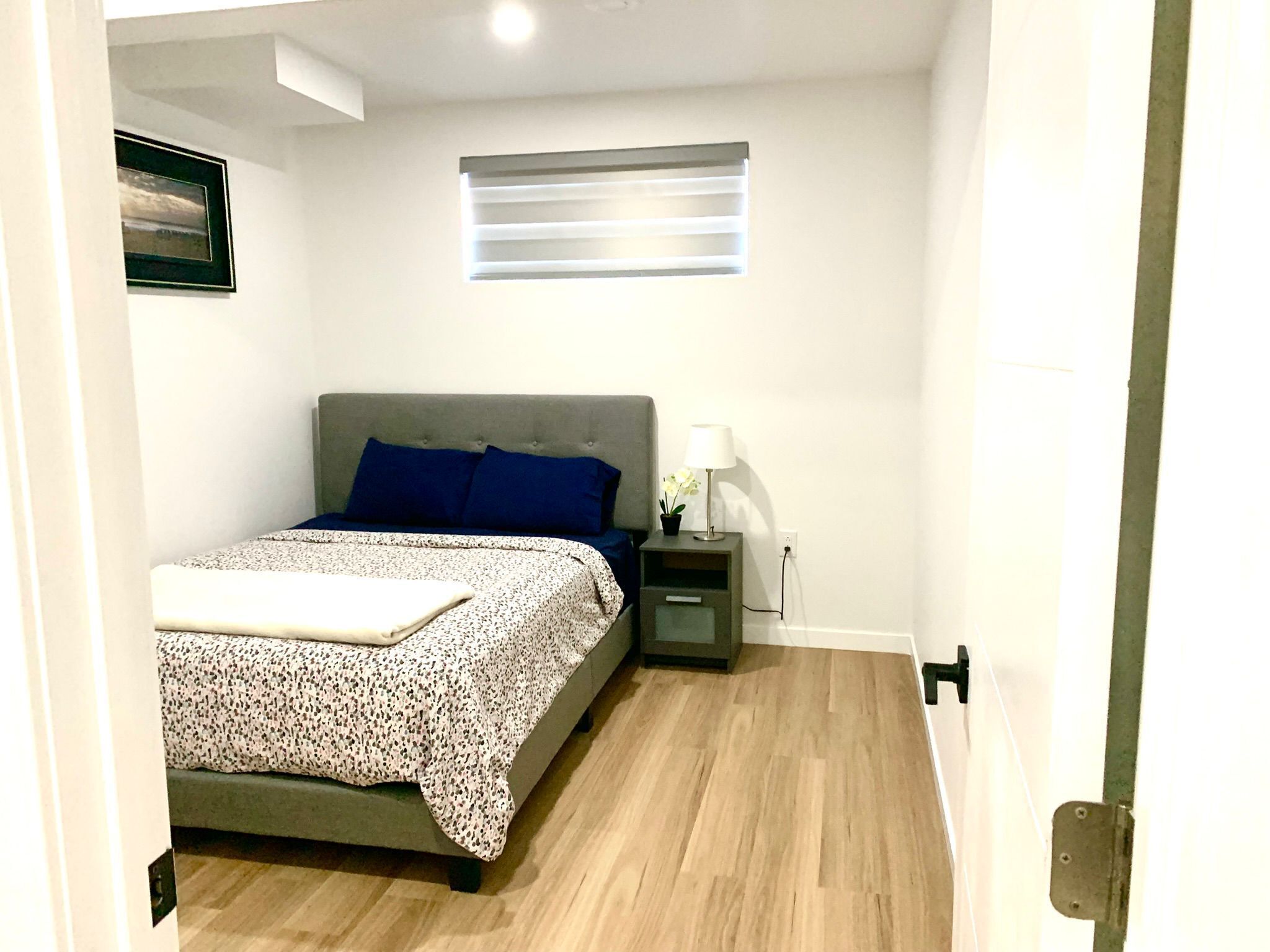 A bedroom with a bed, a nightstand, a lamp, and a window with blinds.