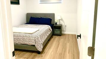 A bedroom with a bed, a nightstand, a lamp, and a window with blinds.