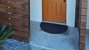 A wooden exterior with a brown door, a black mat at the entrance, and a small plant to the left.