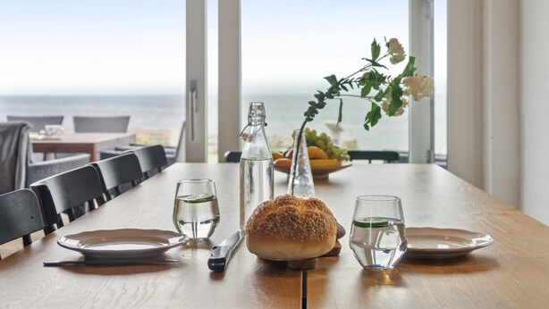 Ett matbord dukat med tallrikar, glas, ett bröd, en flaska och en vas med blommor.