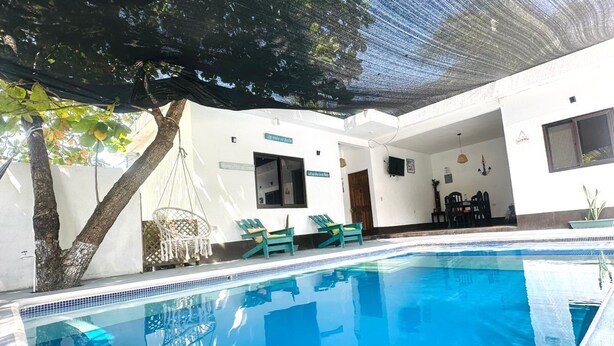 A swimming pool with a tree and lounge chairs, surrounded by a covered patio area.