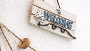 A welcome sign with a nautical theme, including a ship and anchors, hanging on a white textured wall.