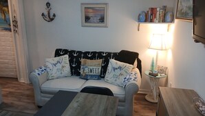 A living room with a sofa, a coffee table, a clock, a framed picture, a lamp, and a bookshelf.