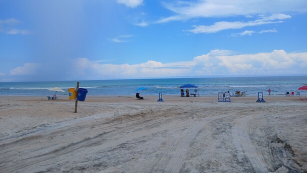 A sandy beach with a clear sky, a few umbrellas, and a sign indicating a lifeguard area.