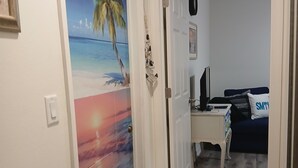 A hallway with a door leading to a bedroom. The bedroom has a bed, a desk, and a chair.