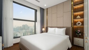 A hotel room with a large bed, a view of the city, a nightstand with a lamp, and a decorative vase. - ARAVELLE SUITES (Hanoi)
