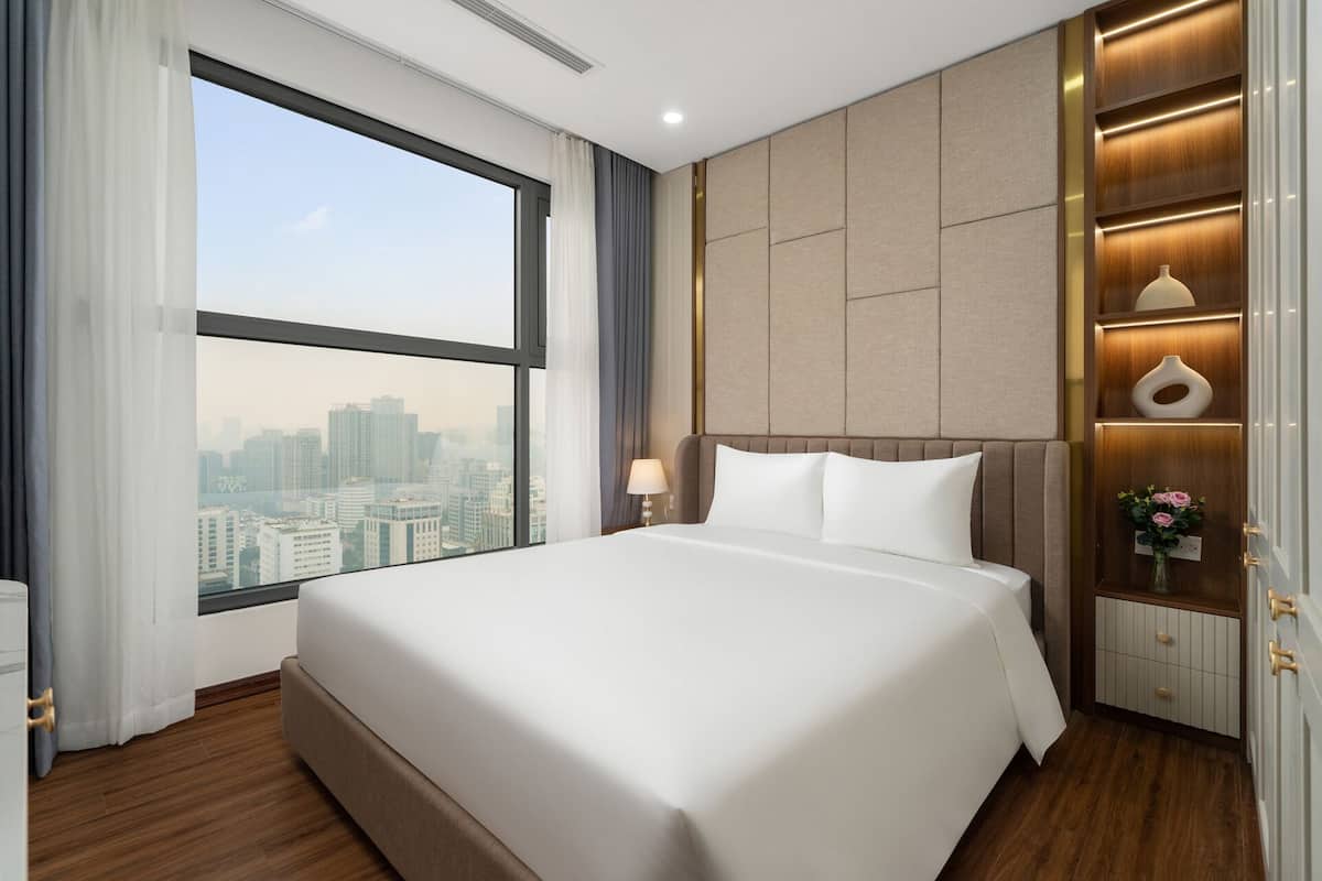 A hotel room with a large bed, a view of the city, a nightstand with a lamp, and a decorative vase.