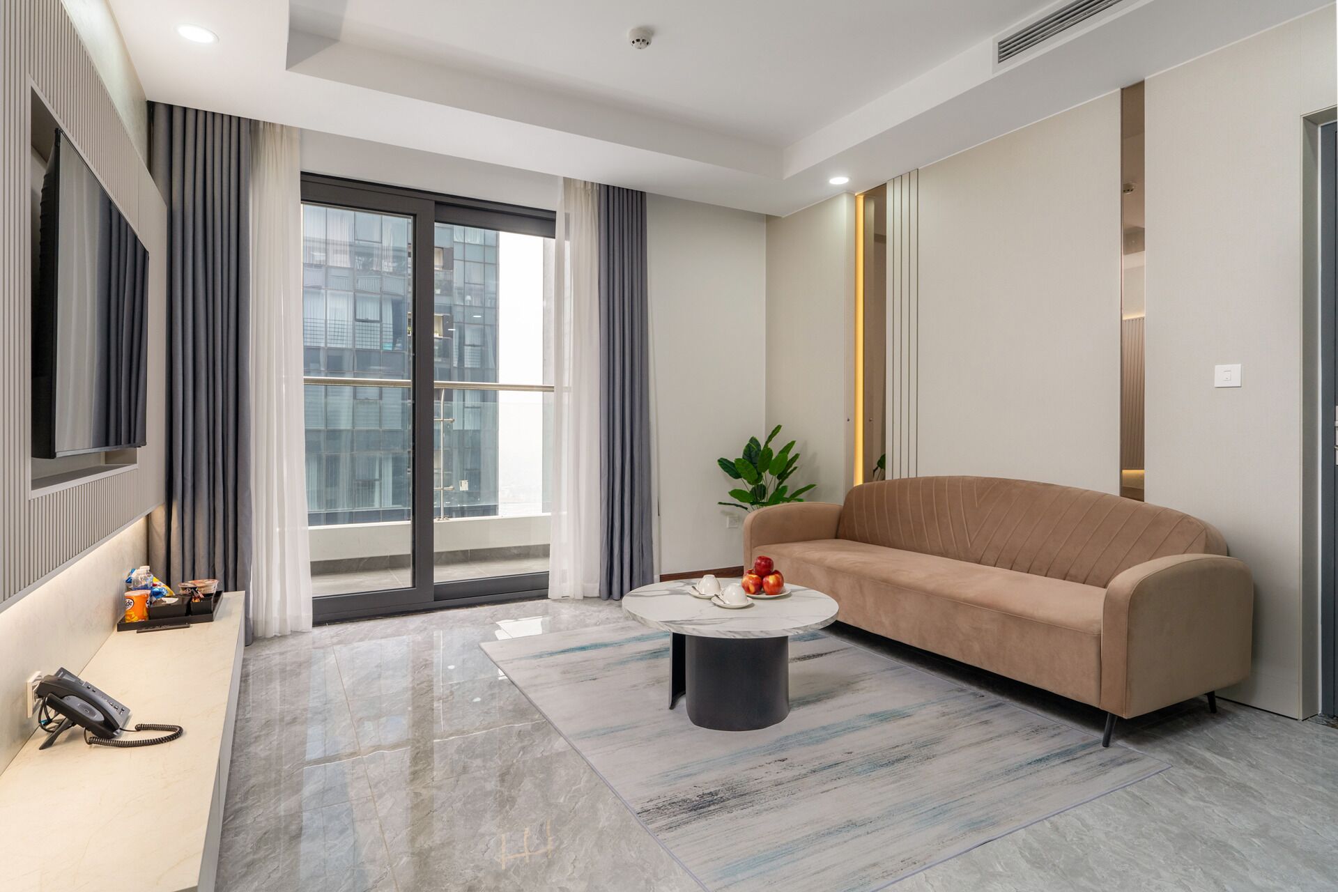 Una sala de estar moderna con un sofá color beige, una mesa de centro redonda y un amplio ventanal con cortinas.