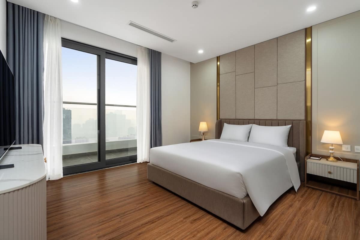 A hotel room with a large bed, two bedside tables with lamps, a view of the city through a large window, and a modern design.
