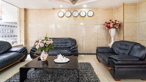 A lobby with two black leather sofas, a coffee table with a vase and teapot, a wall clock, and a flower arrangement.