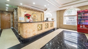 A hotel reception area with a marble counter, a reception desk, a Coca-Cola refrigerator, and a wooden door marked with the number 002.