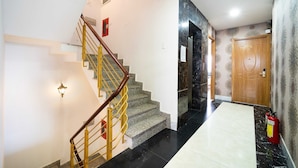 A staircase with a wooden handrail and yellow balusters, leading to a room with a marble floor and a door with a number plate.