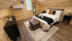 A cozy wooden cabin bedroom with a bed, bedside tables, a desk, and a window.