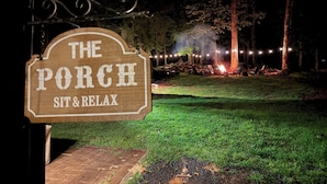 A wooden sign reading "The Porch Sit & Relax" with a view of a lit outdoor area at night.