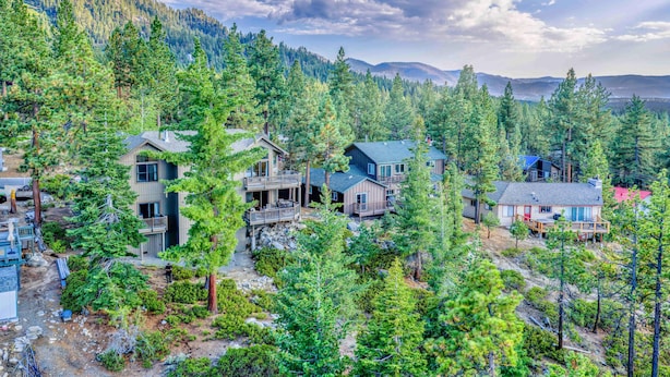 Un quartier résidentiel composé de plusieurs maisons, entouré d’une forêt dense et avec des montagnes en arrière-plan.