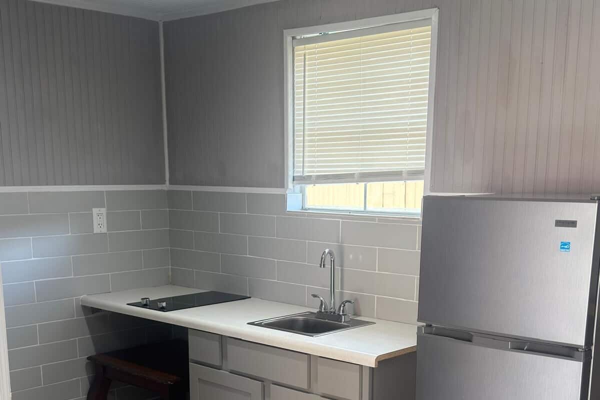 A compact kitchen with a built-in sink, a stainless steel refrigerator, and a window above the sink.