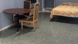 A small room with a round wooden table and two chairs, a bed with a beige bedspread, and a window with a dark curtain. - Star Motel (Tampa)