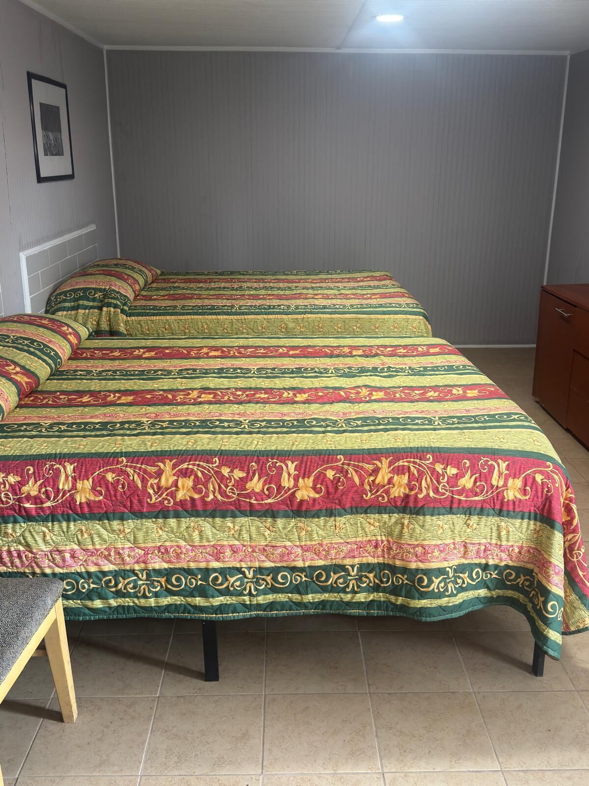 Ein Schlafzimmer mit einem großen Bett, das mit einem gemusterten Bettbezug bezogen ist, einem Nachttisch aus Holz und einer Kommode.
