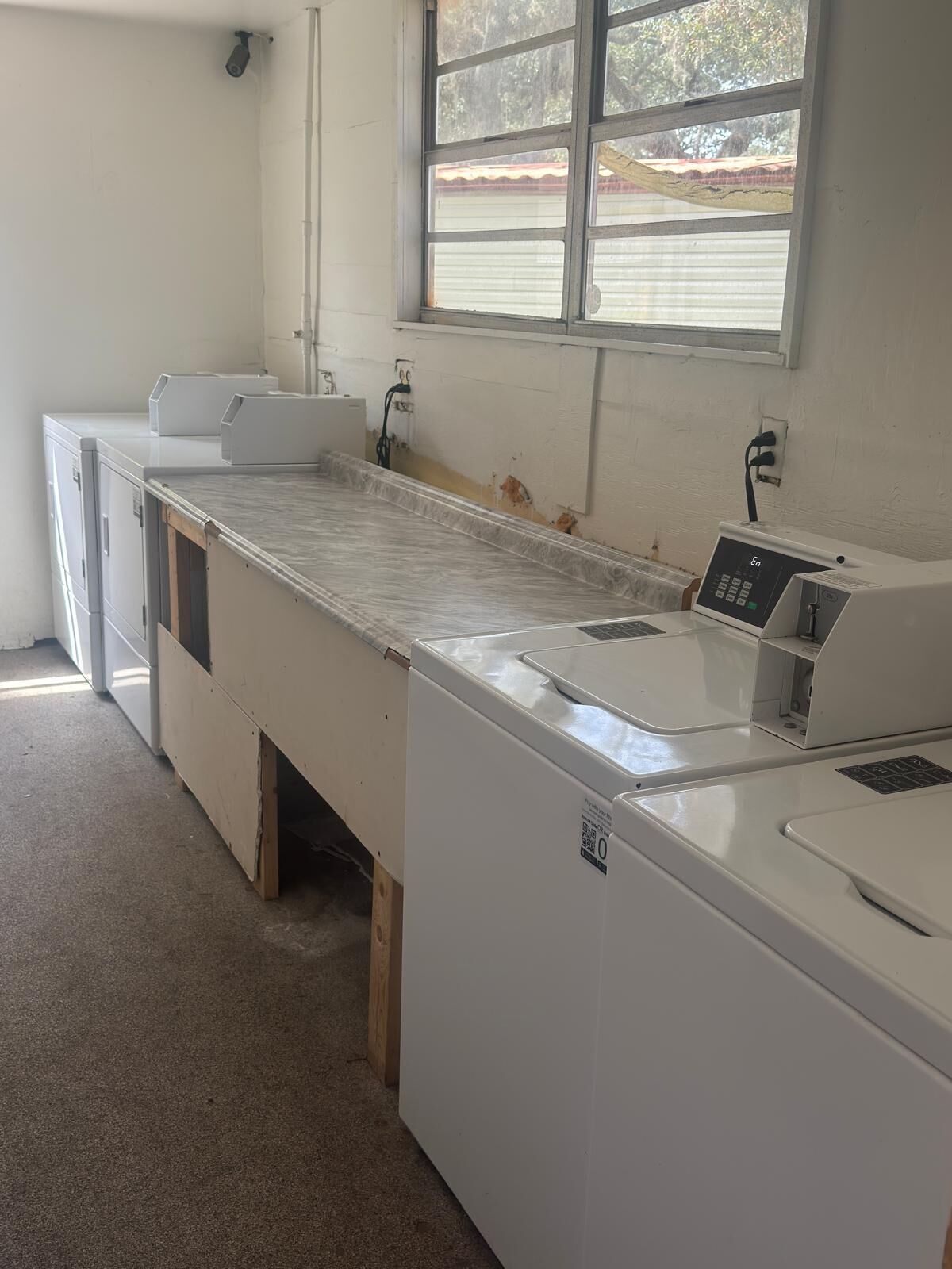 A laundry room with a large industrial washing machine, a smaller dryer, and a countertop with a sink.