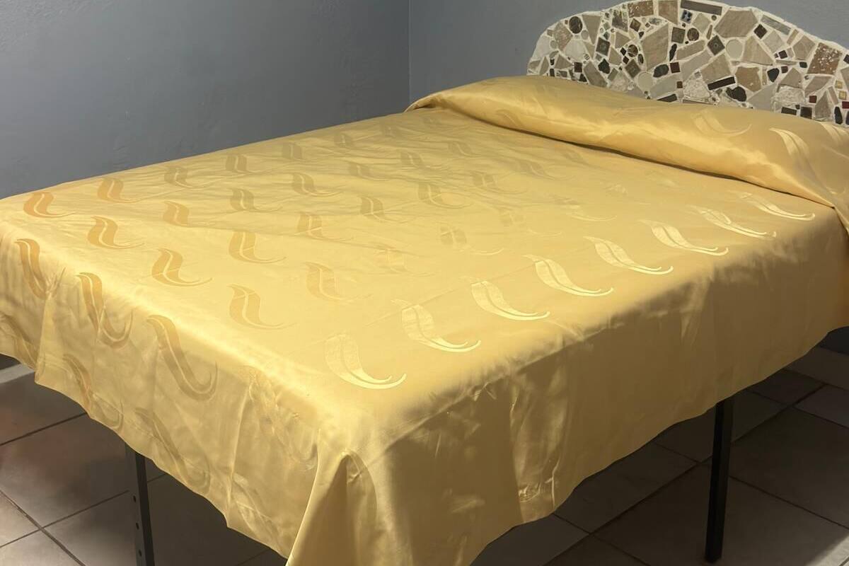 A bed with a yellow bedspread, a headboard with a mosaic design, and a framed picture on the wall.