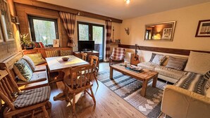 Un salon chaleureux avec une table à manger en bois, un canapé et une table basse. On y trouve également un téléviseur et une guitare posés sur la table.