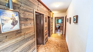 Un couloir intérieur en bois, orné d’une affiche, avec un plancher en bois et un coin repas visible à travers une porte ouverte.