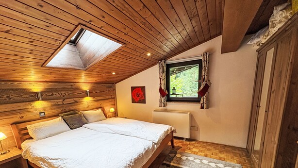 Une chambre avec un plafond en pente, des murs en bois, un grand lit, une fenêtre avec des rideaux et une décoration florale avec une rose rouge.