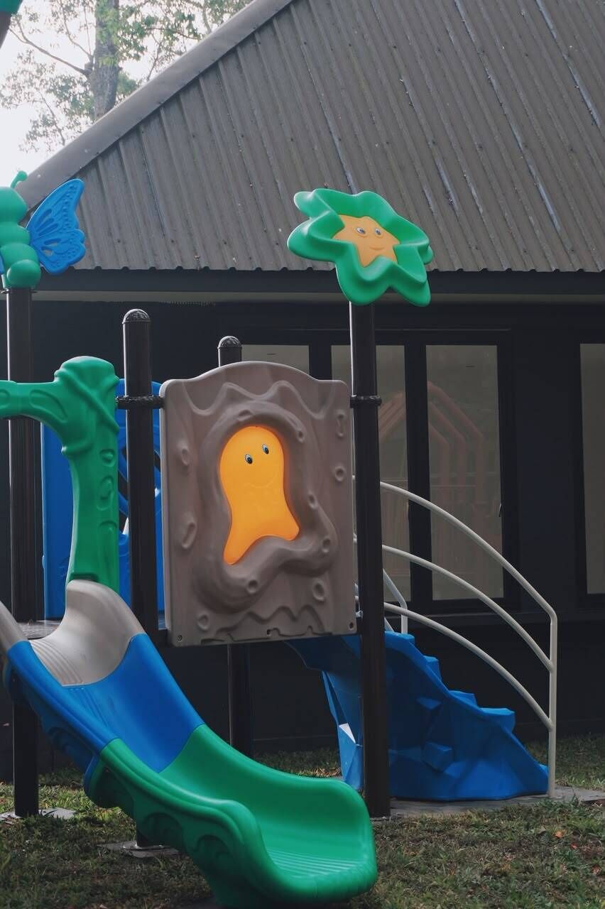 Estructura de juegos infantiles con toboganes y elementos para escalar, frente a un edificio con techo de metal corrugado.