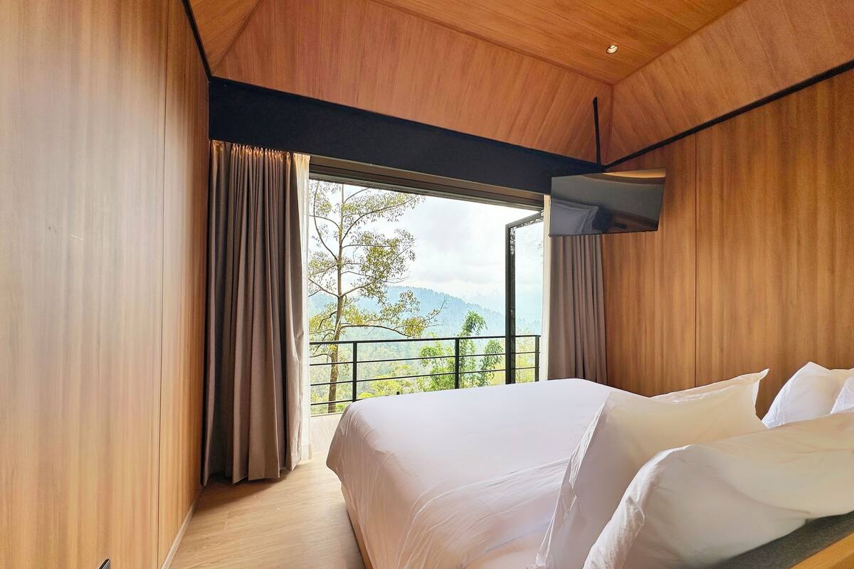 A modern hotel room with a large bed, wooden walls, and a balcony with a scenic view.