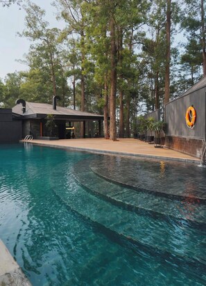 Una piscina de borde curvo, rodeada de árboles y un edificio con fachada oscura y un logotipo amarillo.