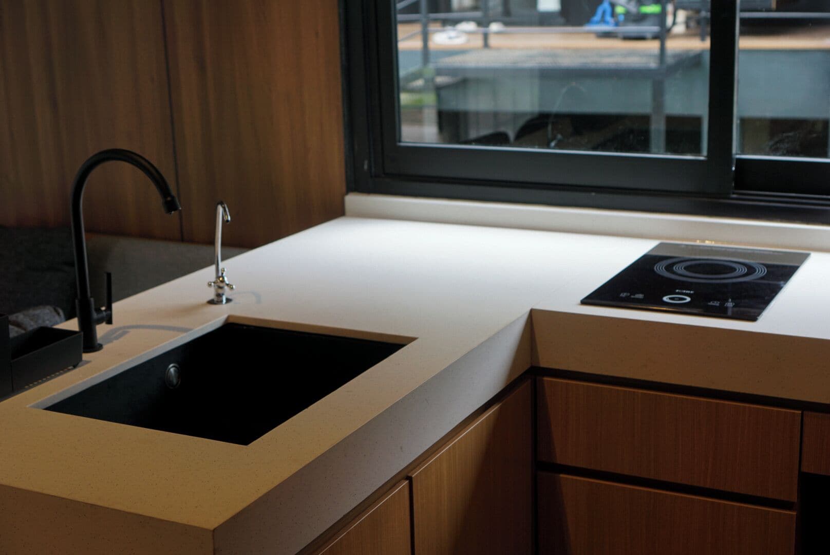 A modern kitchen with a black sink, a window, and a built-in induction cooktop.