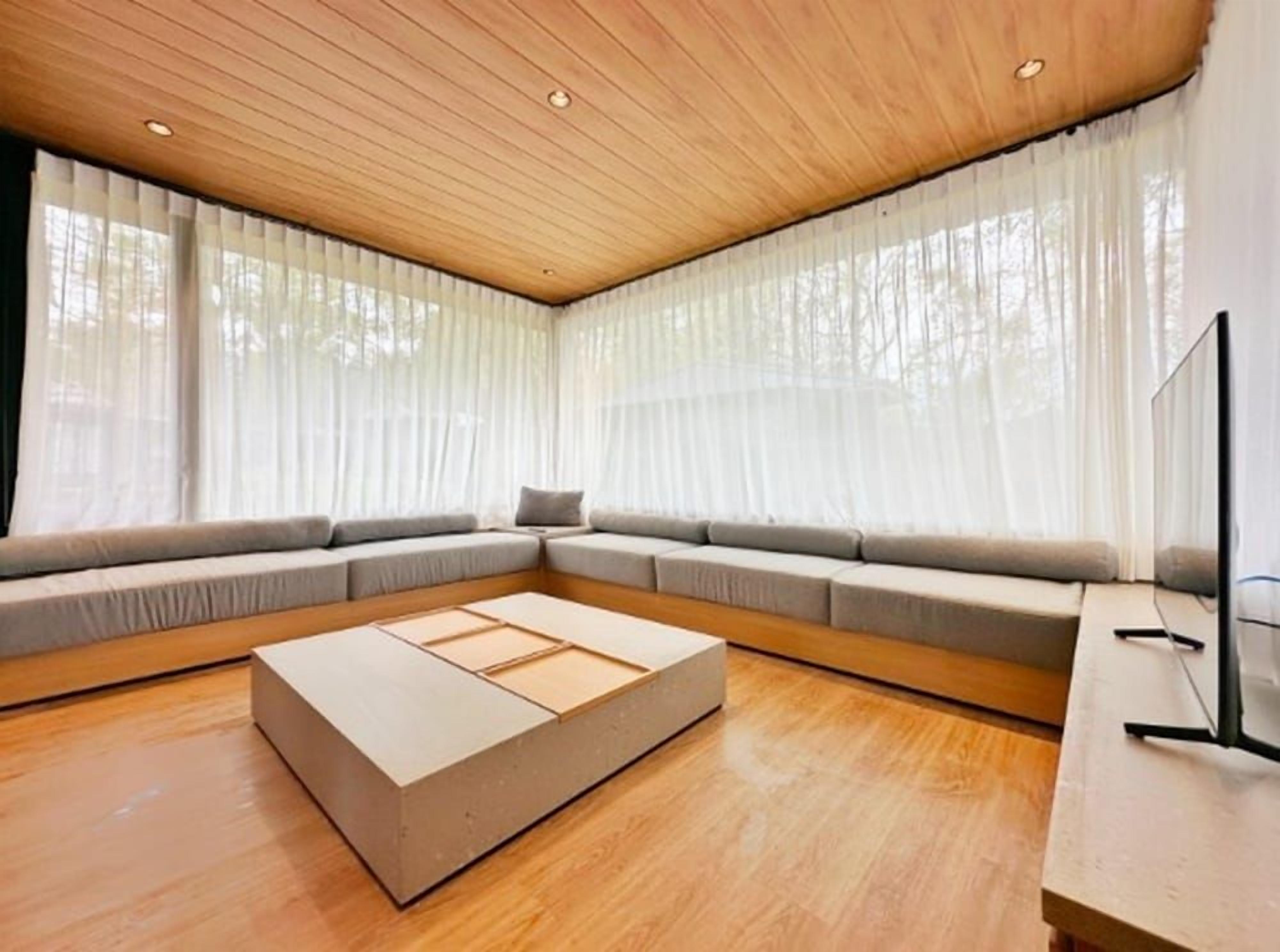 A modern living room with a wooden ceiling, a sectional sofa, a low wooden coffee table, and a television on a stand.