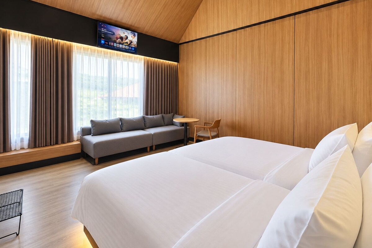 A modern hotel room with a large bed, a sofa, a small table, and a TV mounted on the wall.