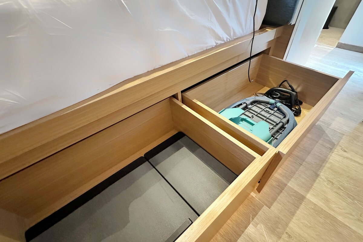 A wooden drawer unit with a mattress and a mattress protector inside.