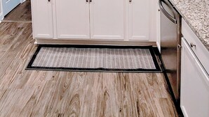 Une cuisine avec des armoires blanches, des comptoirs en granit, un évier en acier inoxydable et un plancher en bois.