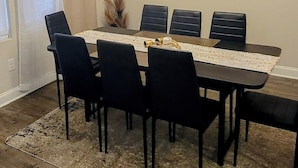 Un coin repas avec une longue table, des chaises noires, un lustre et un tableau encadré au mur.