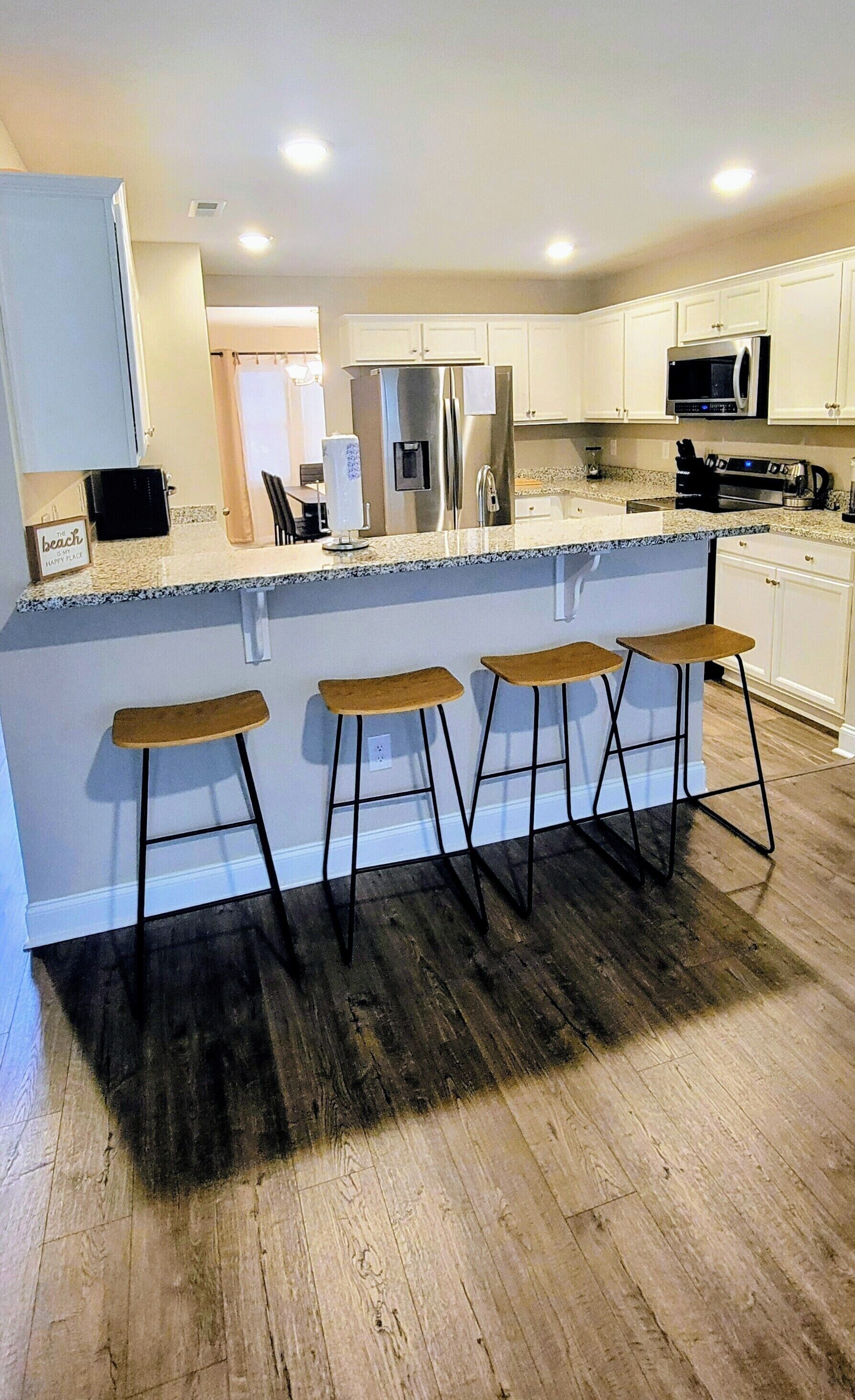 A modern kitchen with a central island, bar stools, stainless steel appliances, and white cabinetry.