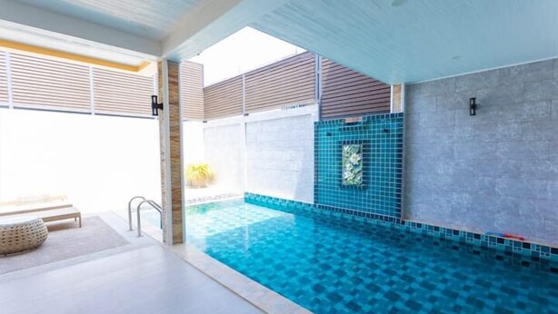 Une piscine intérieure moderne, dotée d’un sol et de murs carrelés, d’une zone de pont en bois et d’un banc pour s’asseoir.