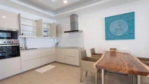 Une cuisine moderne avec des meubles blancs, un four encastré et un coin repas comprenant une table en bois et des chaises en osier.