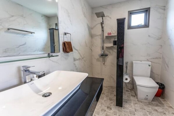 A modern bathroom with a large mirror, a white sink, a shower, and a toilet.