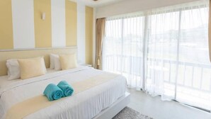 Une chambre d’hôtel dotée d’un grand lit, offrant une vue sur la ville à travers de fines rideaux, et présentant un design moderne avec des murs jaunes et blancs.