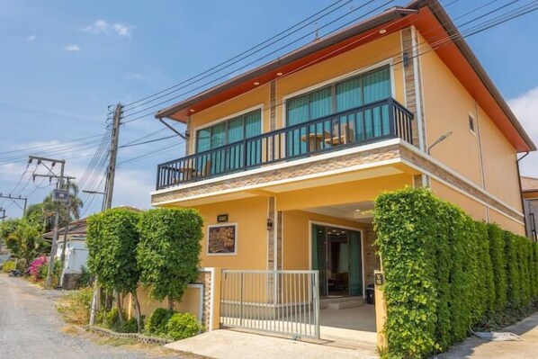 A two-story building with a balcony, a gated entrance, and a well-maintained garden.