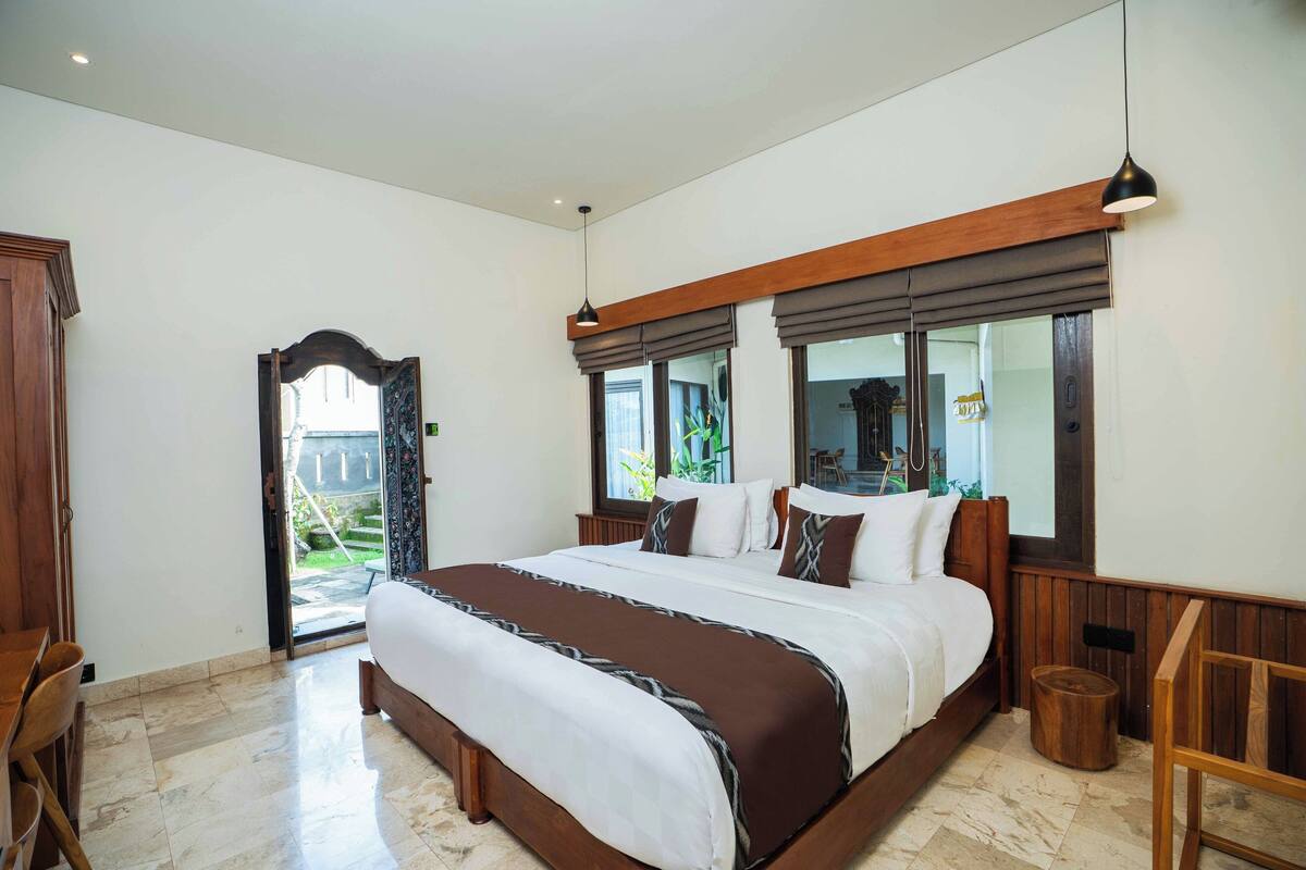 A spacious bedroom with a large bed, wooden headboard, and a view of the outdoors through a sliding door.