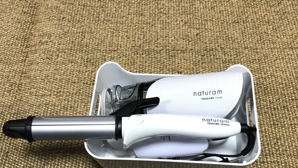 Un sèche-cheveux blanc, portable, doté d’un embout et d’un cordon noirs, présenté dans une mallette de transport blanche sur laquelle on peut voir le nom de la marque, « naturam ».