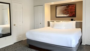 Una habitación de hotel con una cama grande, un espejo, un cuadro en la pared y una puerta.