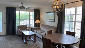 Habitación de hotel con sofá, dos sillones, una mesa de centro, una mesa de comedor y una araña.