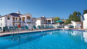 Piscina con sillas de descanso y sombrillas, rodeada de edificios de varios pisos con balcones.