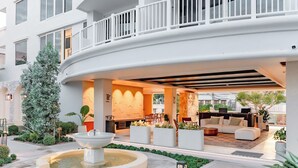 Eine moderne Hotelhalle mit einem gebogenen Balkon, einer Springbrunnen und einer Sitzecke mit Sofas und einem Couchtisch.